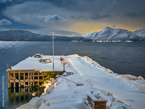 Mestervik, Norway - December 29, 2025: Malangen Brygger Resort. Glowing yellow sky-light on the horizon in the evening cloudscape shows mountain range covered in snow on opposite side of fjord. Hotel 