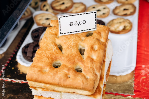 Freshly baked focaccia bread displayed at a market stall with price tag indicating 5,00 alongside various pastries in the background