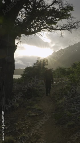 Hiker walking through a forest toward a sunset over the mountains on a stormy day in nature
