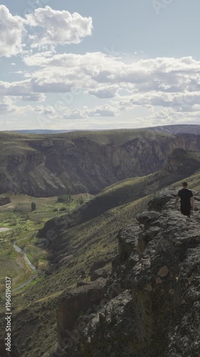 Man walking over on a rocky ledge overlooking canyon vast mountain valley in nature in Parque Patagonia. Santa Cruz, Argentina