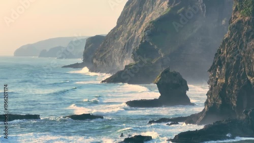 Waves crash against the rugged cliffs and sea stacks of Karekare Beach, New Zealand. The wild, untamed beauty of the coastline is a popular destination for surfers.