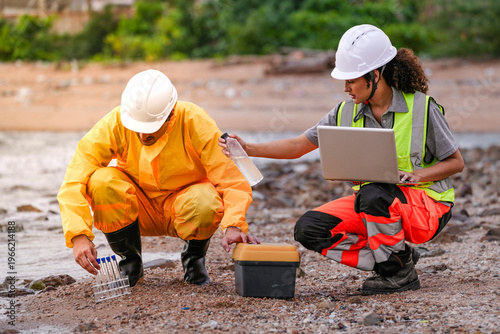 Valokuva Two environmental engineers in safety gear work at a shoreline near gas storage tanks