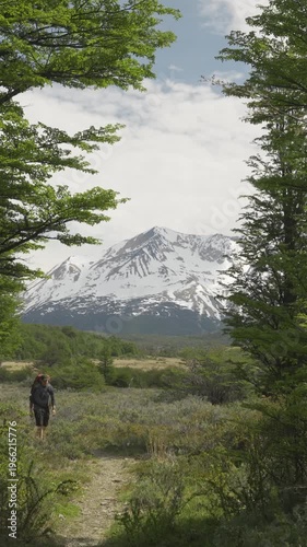 Silhouette of hiker walking in the distance through a forest opening toward snow-capped mountains. Patagonia, Argentina