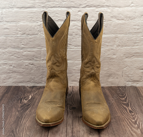 Cowboy boots pair in distressed tan leather on wood floor
