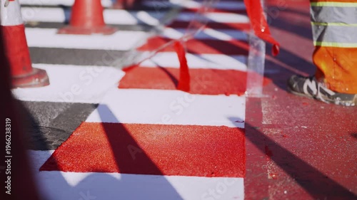 Workers install a new bike path with red thermoplastic coating. Fresh road markings and pedestrian crossings visible. Urban infrastructure upgrade. Sustainable city transport development concept.
