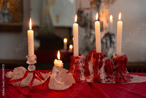 Fotografia Lit candles with dripping red wax on festive red tablecloth