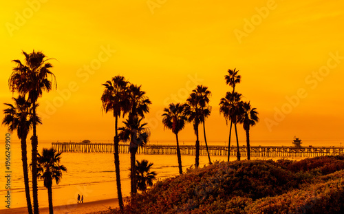 San Clemente Pier at sunset with palm tree silhouettes and golden sky along Southern California coast
