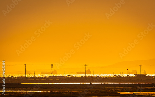 Cargo ships waiting offshore near Long Beach Harbor at sunset with golden ocean and atmospheric haze, Southern California