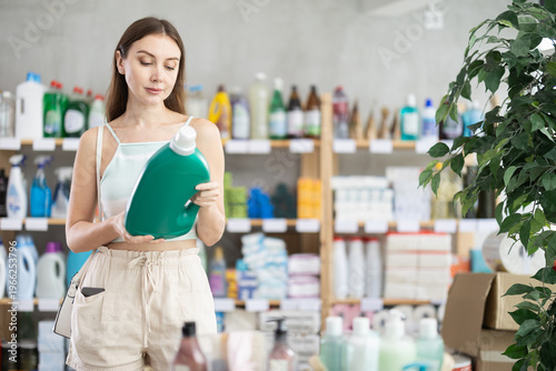 Photos Woman carefully examines label and packaging of liquid detergent while shopping in household store