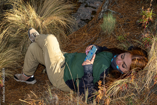 Woman resting on ground checking smartphone while hiking