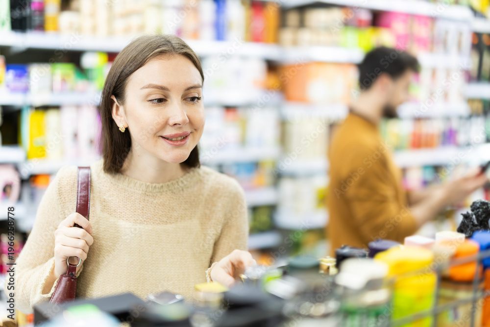 Fototapeta premium Woman buyers chooses shampoo or shower gel in household chemicals store