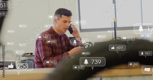 Technician answering call and inspecting bicycle gear for repair at bench, alerts rising around him