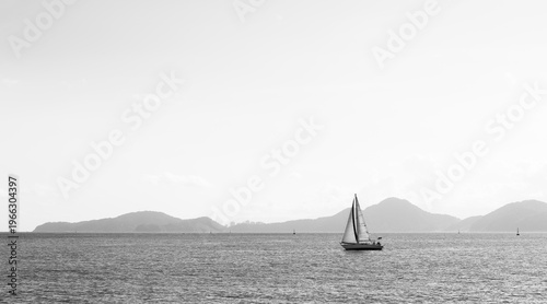 Sailboat on calm sea with mountains in background black and white