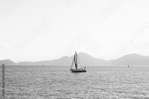 Sailboat on calm sea with mountains in background black and white