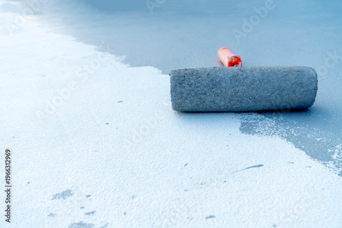 Canvas Print Close-up of a paint roller applying white liquid coating or sealant on a grey industrial floor