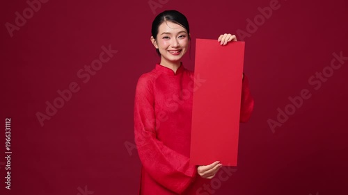 Smiling Asian woman presenting red vertical banner, traditional New Year style, clean red background. Space for design