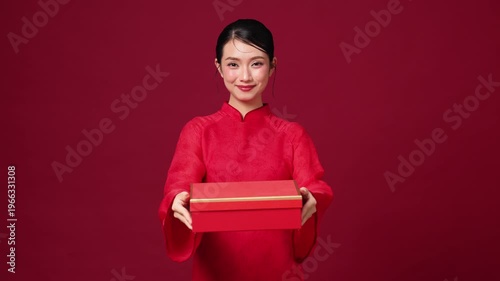Asian woman holding red gift box, warm smile, festive outfit, ideal for holiday gift promotion visuals. Copy space