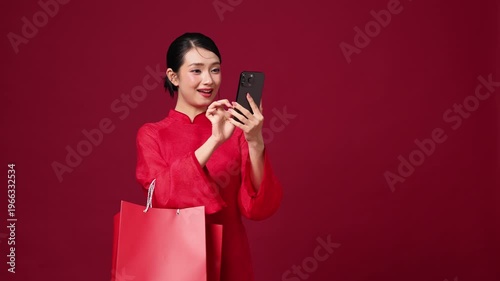 Asian woman smiling and holding shopping bags, festive red background, holiday retail concept.