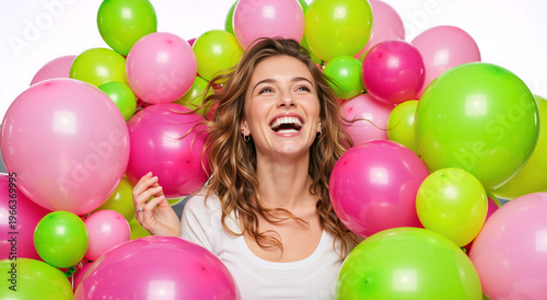 Joyful young woman laughing surrounded by pink and green balloons. Happy female celebrating birthday or party. Cheerful portrait on white background
