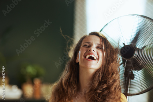 Fotografia A woman with long brown hair, laughing with closed eyes and open mouth, basking in the breeze from a fan