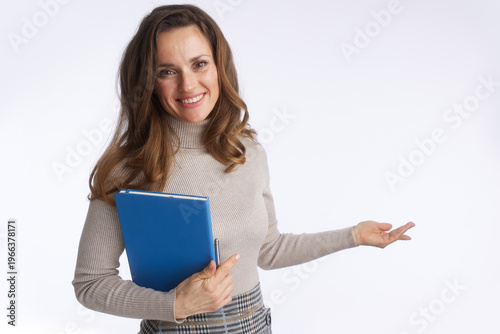 A friendly professional woman holds a blue folder and pen while gesturing to the side, representing a presenter, teacher, or consultant explaining information.