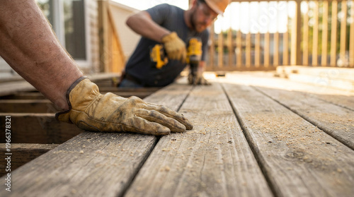 Wallpaper Mural Closeup of a construction workers hand in a work glove resting on wooden deck planks while a colleague uses a drill in the background Torontodigital.ca