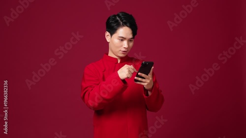 Asian man using a smartphone, a moment of surprise and excitement, wearing red festive attire, a modern New Year's communication theme
