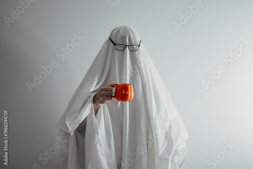 Funny ghost wearing glasses with pumpkin shaped cup against white background.Copy space haloween banner