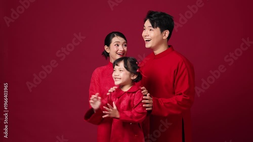 Asian couple with child between them, smiling and clapping, family-focused New Year theme