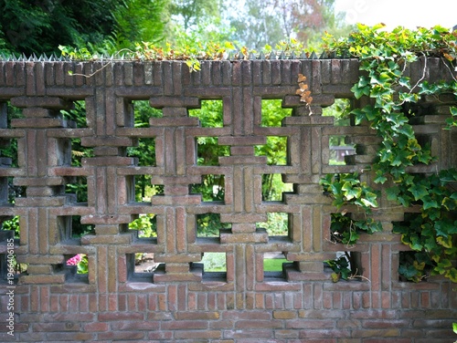 Foto Decorative brick wall with a geometric openwork pattern and green ivy leaves in a bright garden