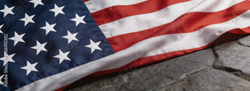 Close-up of the American flag with stars and stripes, partially spread on a stone surface. Depicts national symbol and patriotic themes, showcasing fabric texture and color contrast.