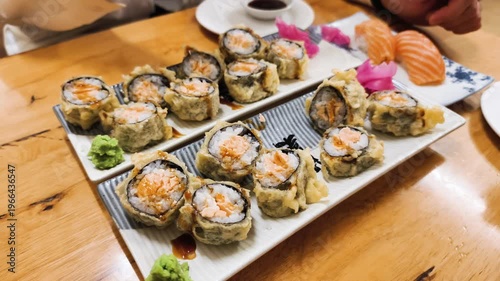 Baked Salmon rolls set features hot sushi with wasabi and ginger on restaurant table. Delicious Japanese cuisine uses Baked Salmon with spicy sauce and tempura for gourmet seafood lunch in cafe.