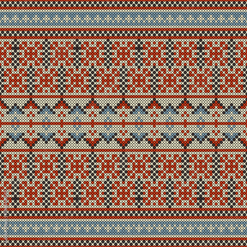 A cross-stitch pattern in a style combining indigenous and geometric motifs, resembling designs found on sweaters or woven fabrics. The color palette includes brick red, muted blue, and cream. 