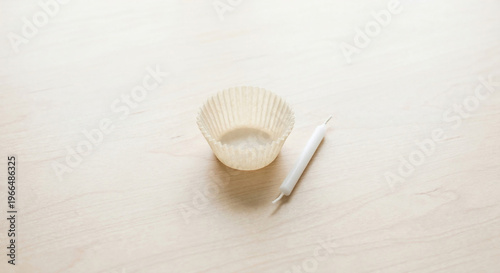 Empty paper cupcake liner and unlit birthday candle on wooden table