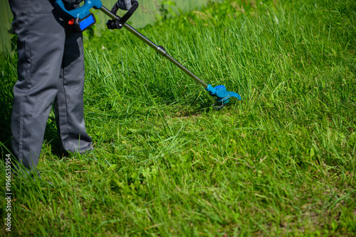 Landscaper trimming grass along fence, close-up. Commercial landscaping, grass mowing.