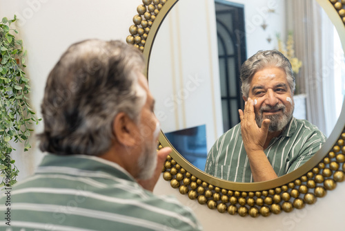 Middle age mature indian man in 50s doing her daily skincare routine, applying face cream to maintain healthy and glowing skin, Senior male self-care and beauty at older age.