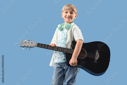 Little boy with headphones and guitar on blue background