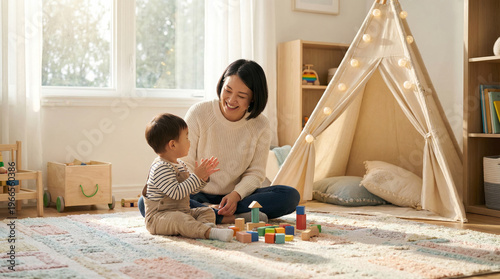 Asian Mother Playing with Toddler Son on Rug in Sunlit Nursery, Loving Parenting Moment