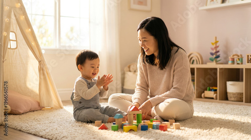 Asian Mother Playing with Toddler Son on Rug in Sunlit Nursery, Loving Parenting Moment