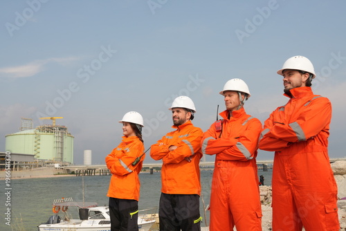 A group of male engineers and their male and female architect colleagues, dressed in uniforms and carrying laptops, stand with their arms crossed, confident of the success of their team inspecting wor