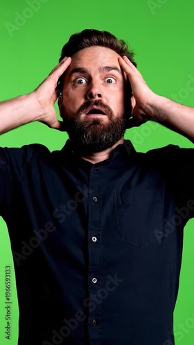 A man with a beard expresses shock and disbelief, holding his head in his hands against a vibrant green background