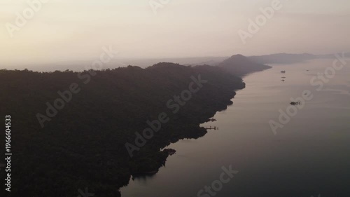 High altitude aerial footage of mountain ridge along the jagged coastline of the Nam Ngum Lake during late afternoon hours with hazy polluted air in the background.