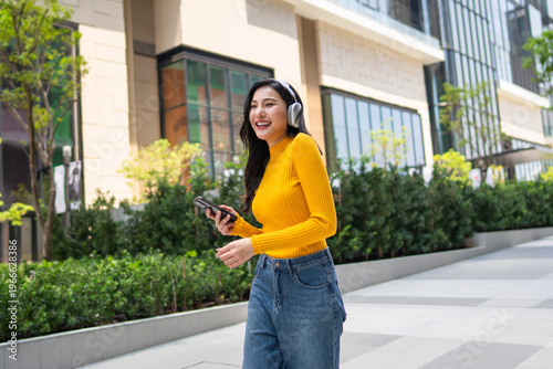 Asian woman enjoying music with headphones while standing in the city.