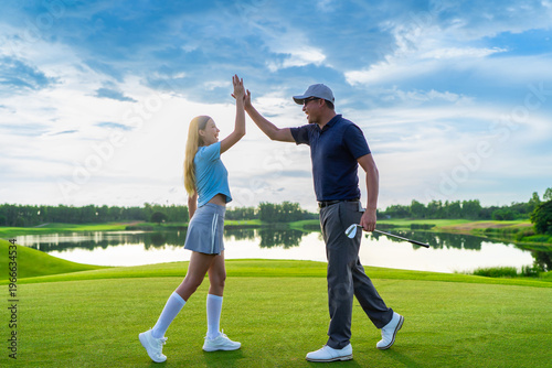 Asian man and woman golfers making a high five on scenic golf course. 
