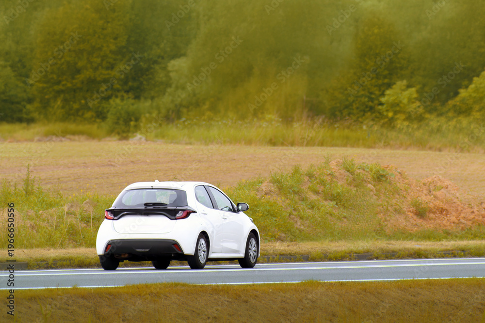 Fototapeta premium Urban hatchback driving through open green fields
