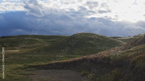 Sunbeams shine on wild hills with feather grass swaying in the wind through thunderclouds.