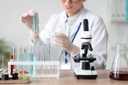 Microscope on table against female scientist with glassware working in labora...