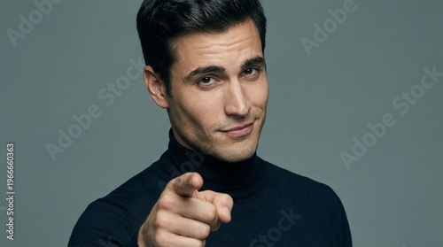 A confident and stylish man in a dark turtleneck points directly at the camera with a subtle, knowing smirk.