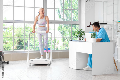 Male physiotherapist working with mature woman on treadmill in rehabilitation...