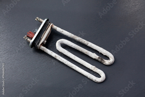 A burned heating element from a washing machine is shown on a dark surface. The element is damaged and shows signs of wear and damage from use.